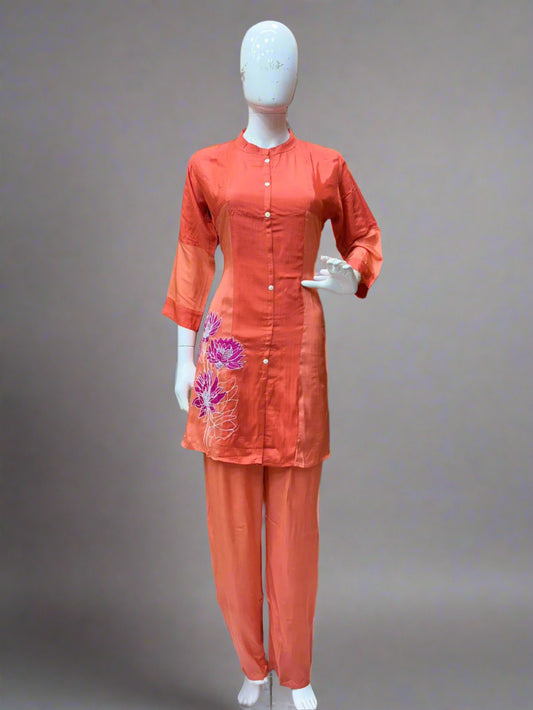 Mannequin wearing an orange outfit with floral embroidery in a room setting.